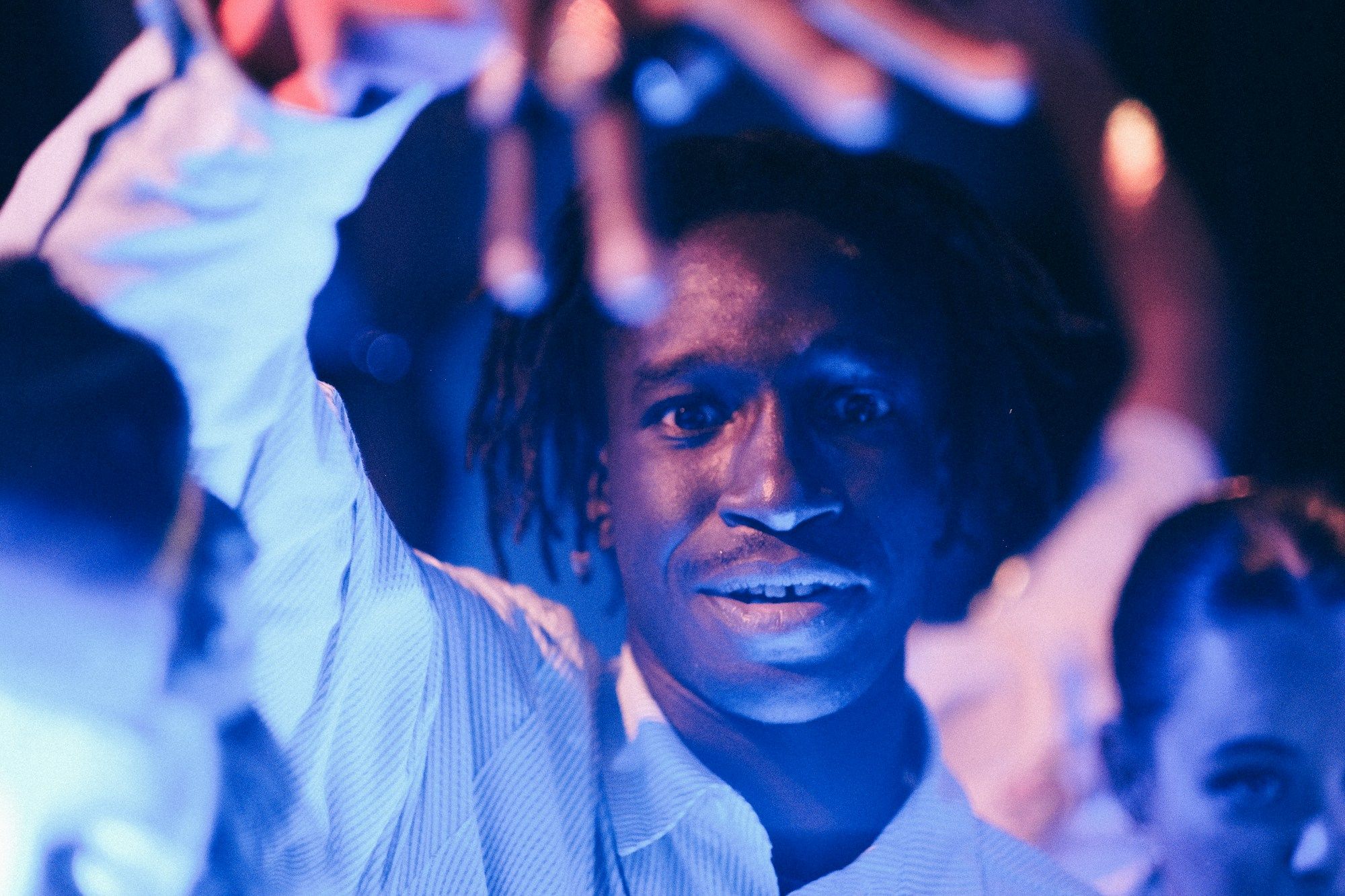A man with his hands up in a crowd under blue party lights