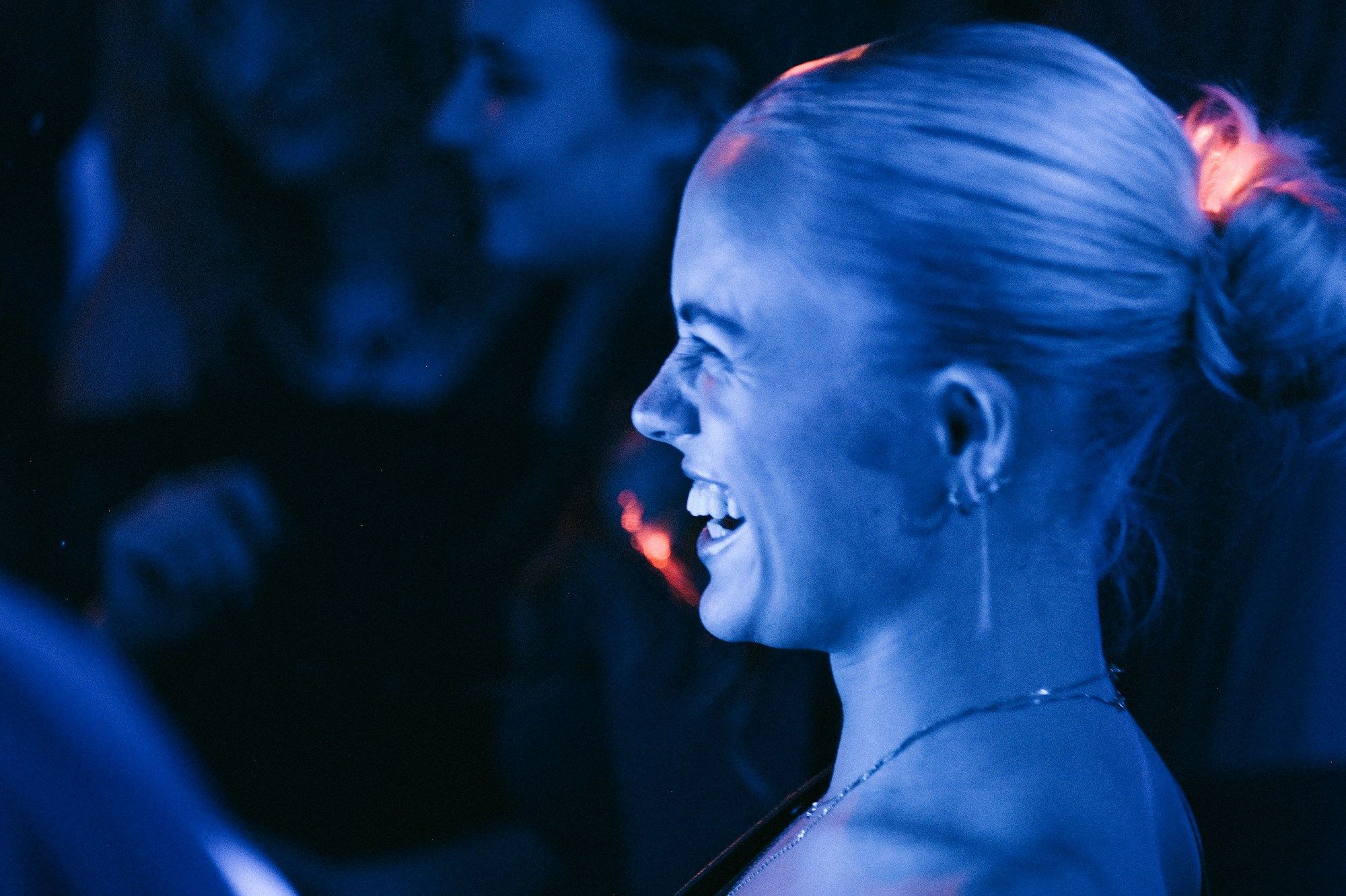 A woman in profile at a party lit in deep blue